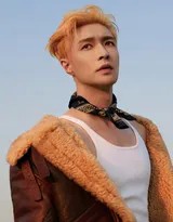 张艺兴身着白色背心倚靠机车，手臂与腹部的肌肉线条紧绷而清晰，展现出力量感，背景是辽阔的天空与旷野。