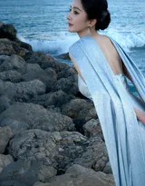 赤足漫步于潮水边缘，湛蓝裙裾浸入清澈海水中，与自然相融，仿佛大海为她延伸出的华丽一部分