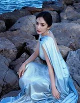 侧身凝望远方，礼服的扭结抹胸设计精巧勾勒出优越的肩颈与背部线条，碎钻如星辰洒落于海浪之上