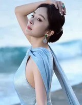 杨幂身披如海浪般流动的湛蓝缎面礼服，于沙滩上翩然转身，裙摆划出优雅弧线，身后是辽阔无垠的海洋