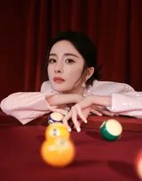 杨幂手持台球巧粉，低头轻抹杆头，卷发垂落，侧颜在光影中显得精致而温柔，展现了准备时刻的宁静与专业