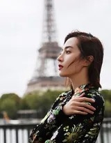 胡冰卿身着黑色印花旗袍，于巴黎街头凭栏远眺，古典雅韵与都市背景交织如画