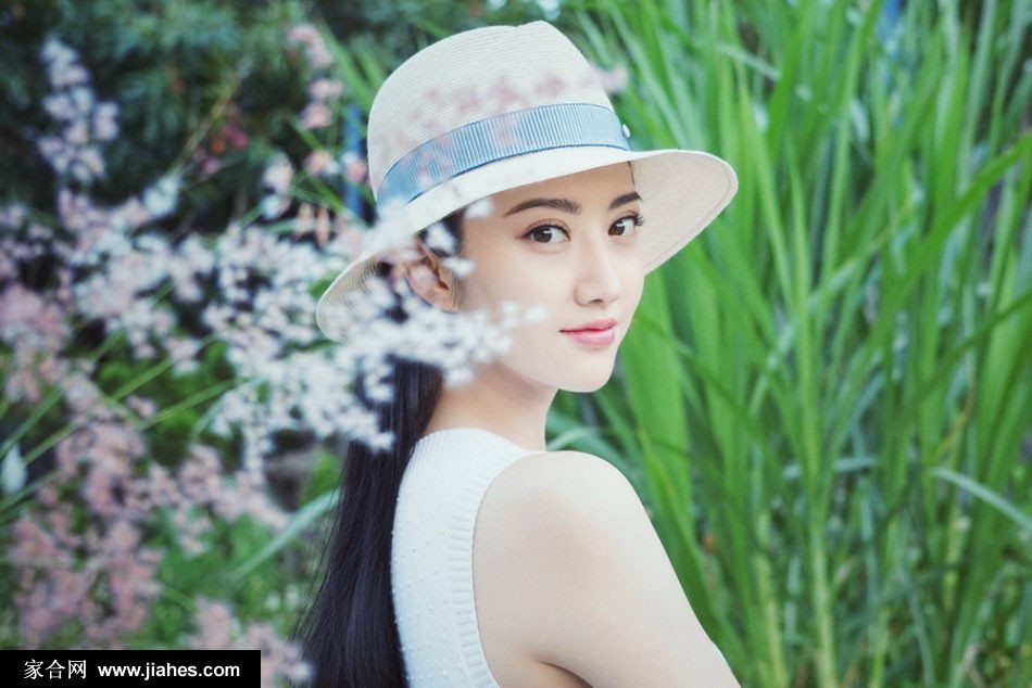 景甜头戴宽檐草帽立于海边，海风轻拂她的白色裙摆与发丝，眼神恬静眺望远方