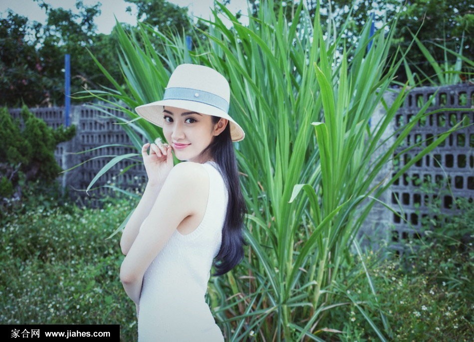 景甜手持草帽微微低头，发丝垂落，神情温柔娴静，仿佛在聆听海浪低语