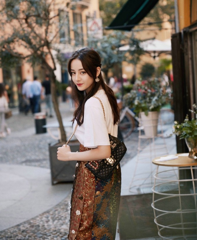 迪丽热巴倚靠复古砖墙，米色毛衣与温柔卷发在秋日阳光下闪耀