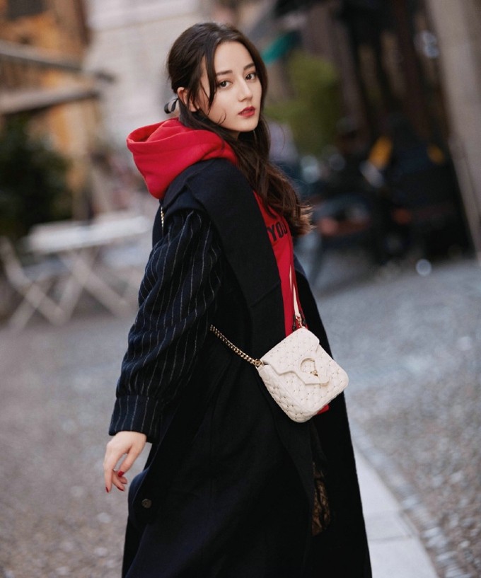 热巴侧身回眸浅笑，格纹大衣随风轻扬，发丝间洒落斑驳光影