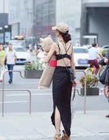 美女倚靠复古墙壁，手拿布偶，吊带内衣凸显曼妙曲线，街头背景增添生活气息