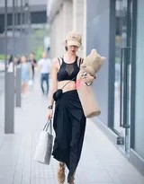 时尚美女手持可爱布偶，身着黑色吊带内衣，在街头自信漫步，阳光洒在她的肩上