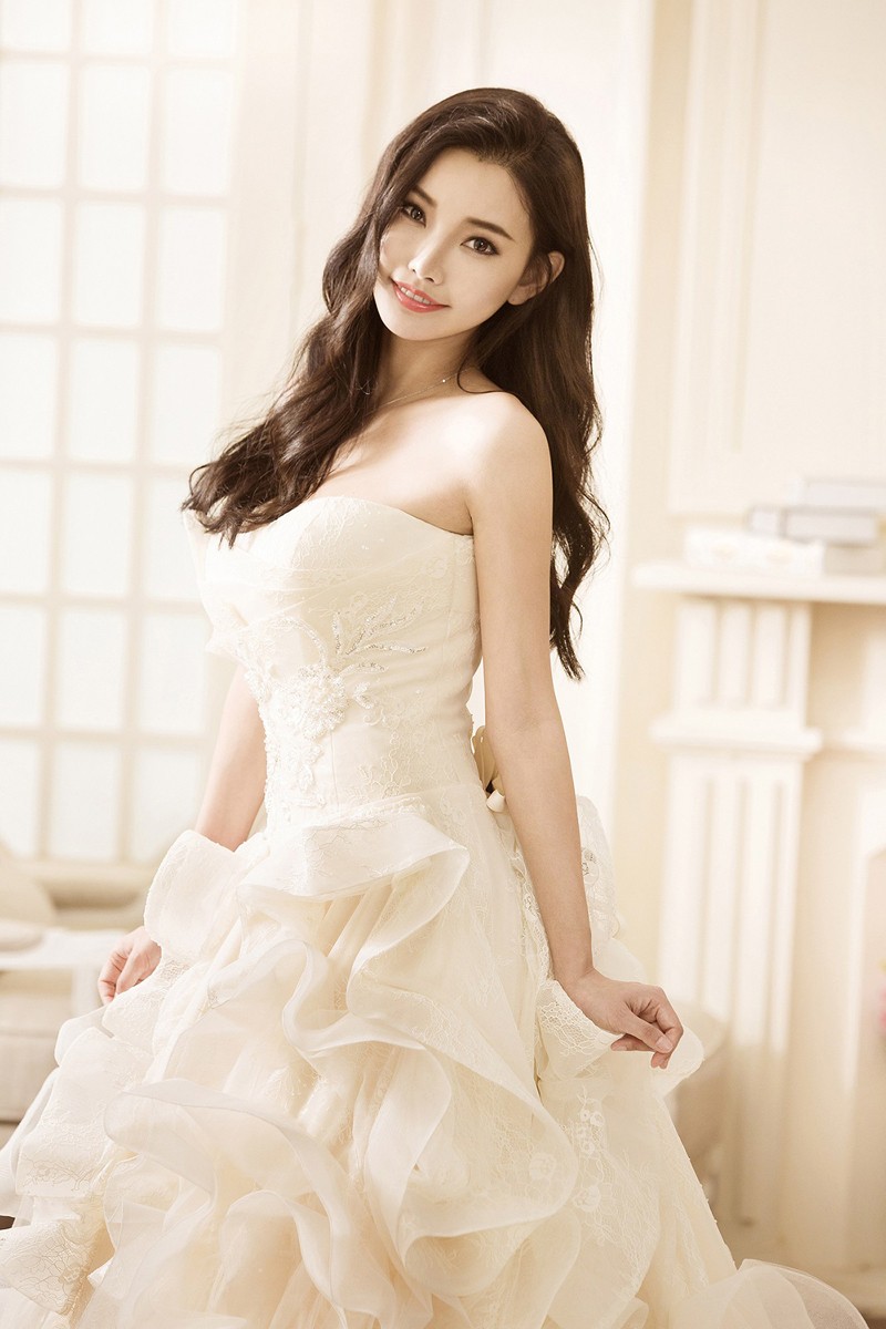 童菲身披一袭华丽蕾丝拖尾白纱，于光影间回眸浅笑，宛如从童话中走出的仙子