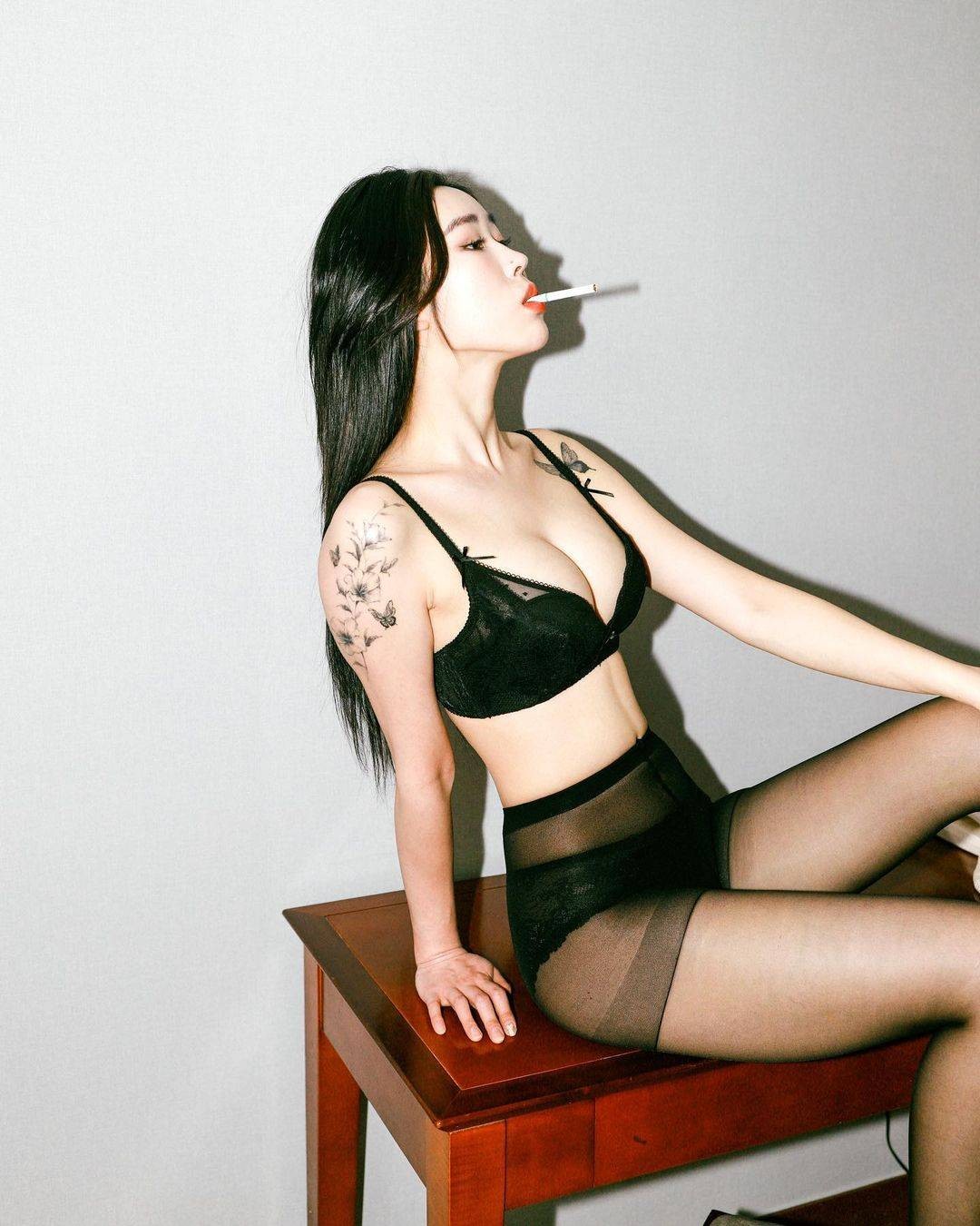 暗调光影下，模特指尖轻夹香烟，烟雾缭绕中眼神疏离，黑色丝袜勾勒出完美腿部线条