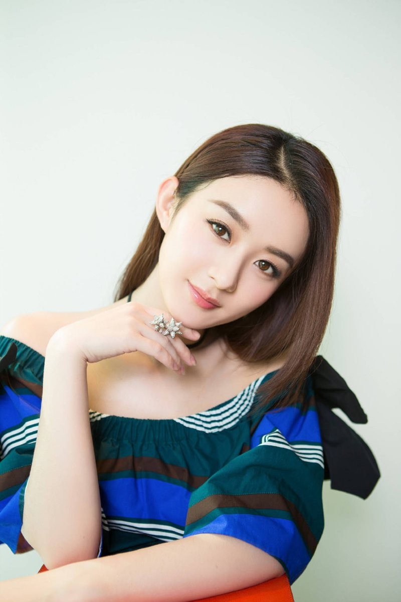 赵丽颖身着浅粉色针织衫，手持花朵侧身浅笑，眼神温柔似水，背景虚化的光斑如星点般浪漫。