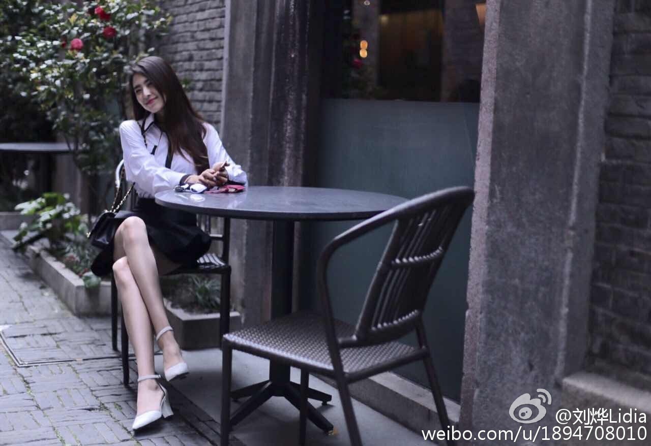 刘烨手持咖啡杯走在街头，步履轻盈，风衣与裙摆随风摆动，展现都市女性的从容姿态