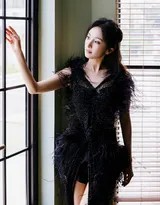 杨幂靠坐于木质柜前，黑色羽毛礼服的纹理在灯光下清晰可见，渔网袜为造型增添一抹不羁的性感